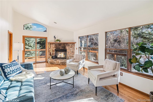 living room with a stone fireplace, vaulted ceiling, and wood finished floors