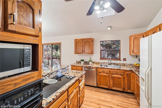 kitchen with light wood-type flooring, black appliances, a sink, brown cabinetry, and light stone countertops