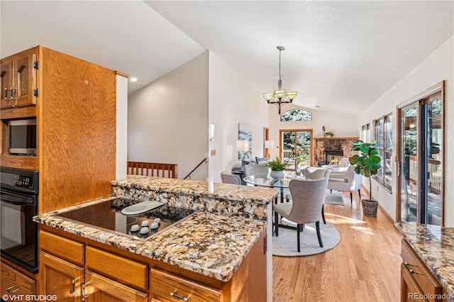 kitchen with brown cabinetry, black appliances, vaulted ceiling, light wood-style floors, and open floor plan