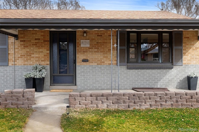 entrance to property with brick siding, a porch, and roof with shingles