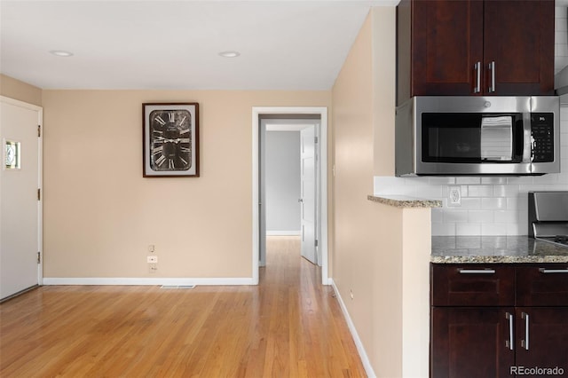 kitchen with stainless steel microwave, baseboards, light wood-type flooring, and backsplash