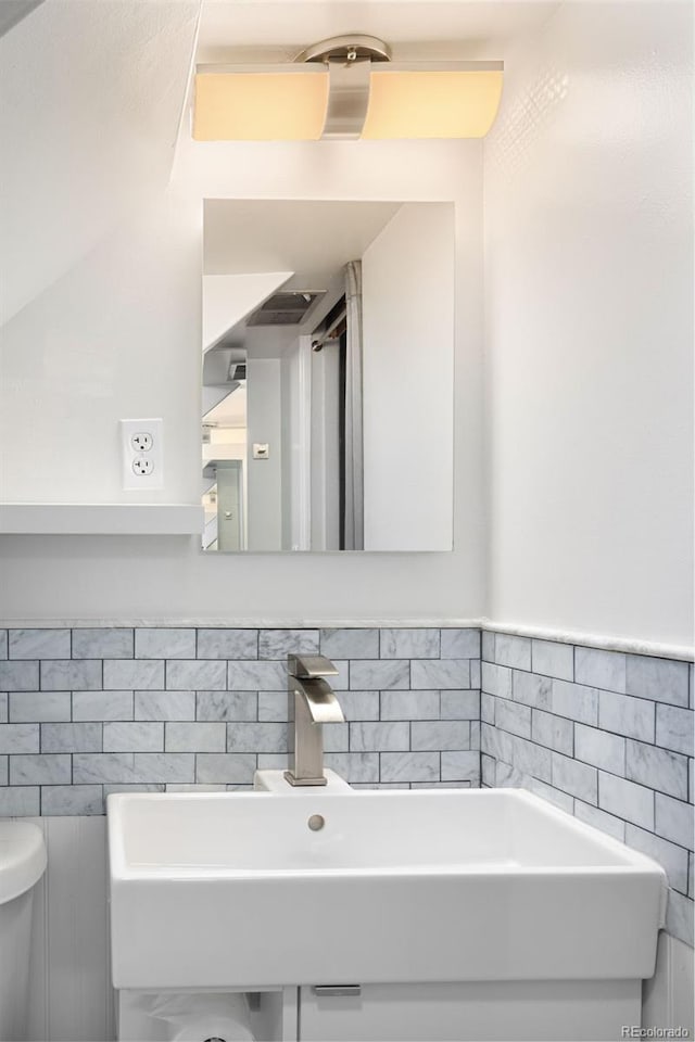 bathroom with toilet, tile walls, and a sink