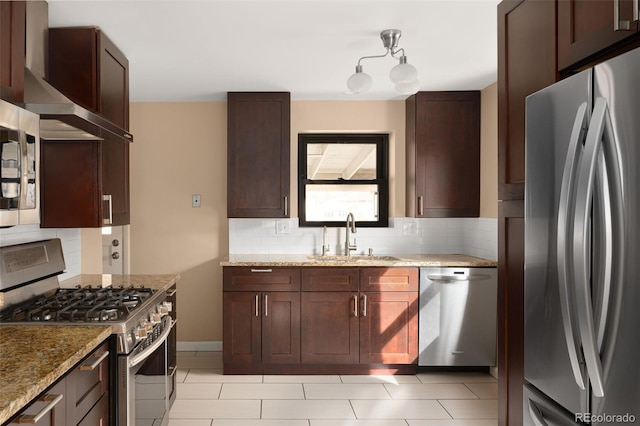 kitchen featuring light stone countertops, a sink, appliances with stainless steel finishes, wall chimney exhaust hood, and tasteful backsplash