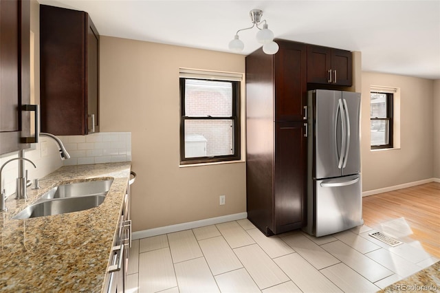 kitchen with a sink, tasteful backsplash, freestanding refrigerator, dark brown cabinetry, and light stone countertops