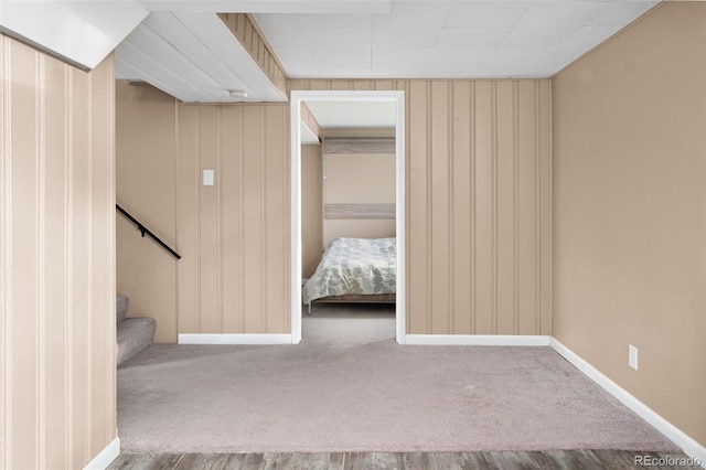 unfurnished bedroom with baseboards, carpet floors, and wood walls