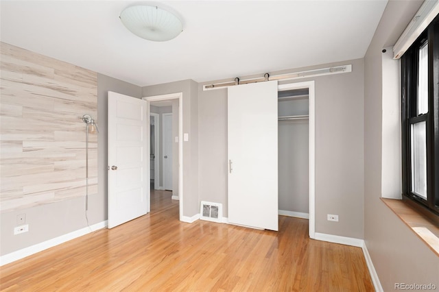 unfurnished bedroom with light wood-type flooring, visible vents, baseboards, and a barn door