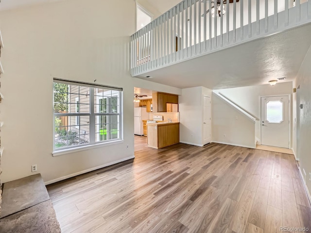 13598 E Asbury Dr, Aurora, CO 80014 - unfurnished living room featuring light wood-style floors, a high ceiling, baseboards, and stairs
