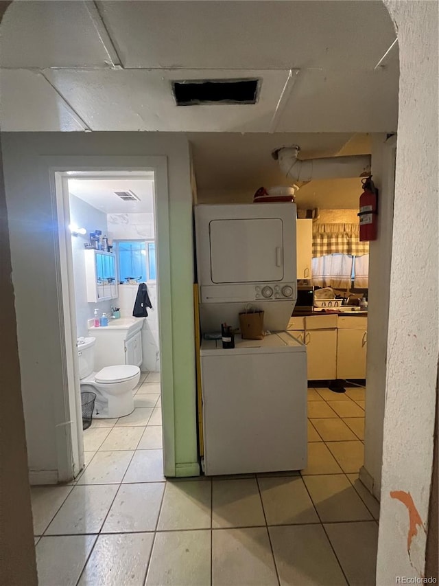 laundry area with light tile patterned floors and stacked washing maching and dryer