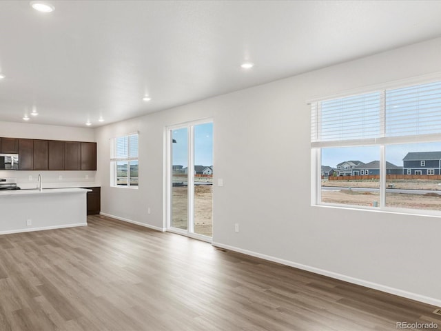 unfurnished living room featuring light wood-style flooring, recessed lighting, baseboards, and a sink