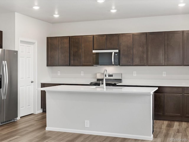 kitchen featuring appliances with stainless steel finishes, light wood-type flooring, a kitchen island with sink, light countertops, and recessed lighting