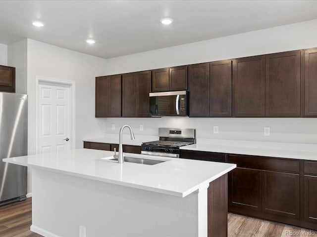 kitchen featuring stainless steel appliances, a sink, light wood finished floors, light countertops, and dark brown cabinets