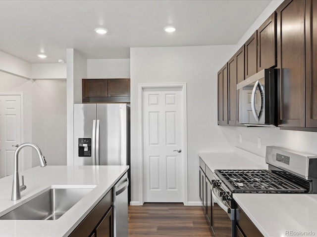 kitchen with appliances with stainless steel finishes, a sink, dark brown cabinets, dark wood finished floors, and light countertops