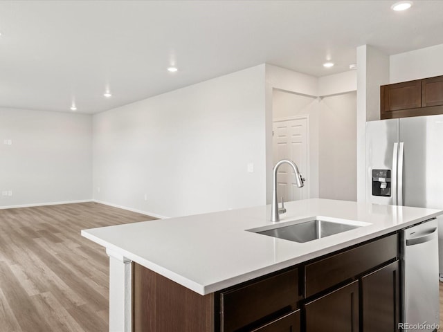 kitchen featuring a sink, a center island with sink, light wood finished floors, recessed lighting, and light countertops
