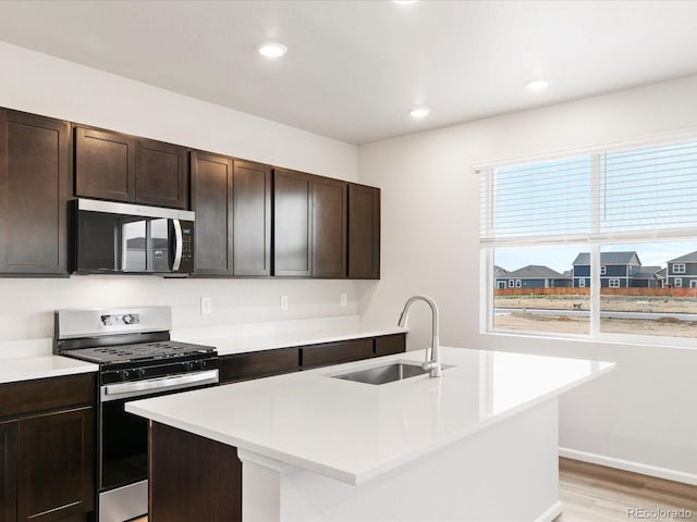kitchen with stainless steel appliances, a sink, light countertops, light wood finished floors, and dark brown cabinets