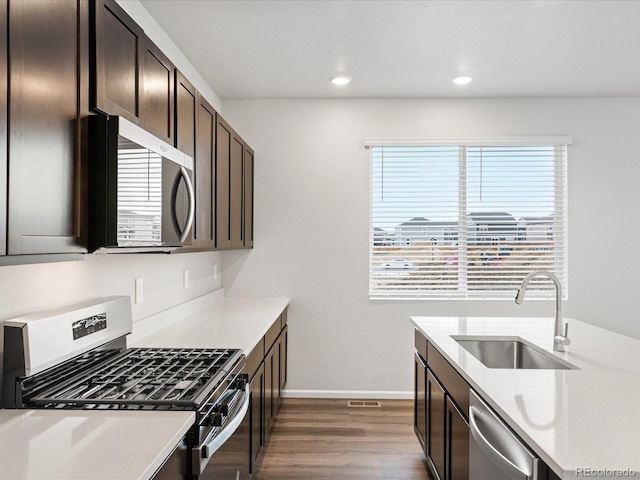 kitchen featuring appliances with stainless steel finishes, a sink, dark wood-style flooring, dark brown cabinetry, and light countertops