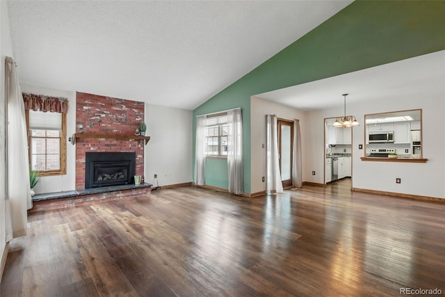 unfurnished living room featuring healthy amount of natural light, wood finished floors, a fireplace, a chandelier, and high vaulted ceiling