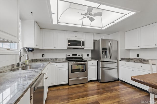 kitchen with appliances with stainless steel finishes, a sink, light stone countertops, and dark wood-style floors