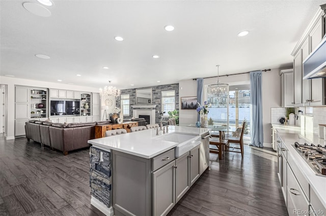 kitchen with a kitchen island with sink, gray cabinetry, hanging light fixtures, a notable chandelier, and dark hardwood / wood-style flooring