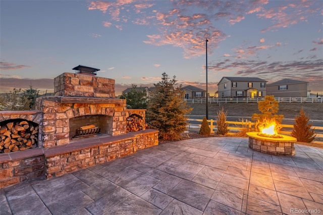 patio terrace at dusk featuring an outdoor fire pit and an outdoor stone fireplace