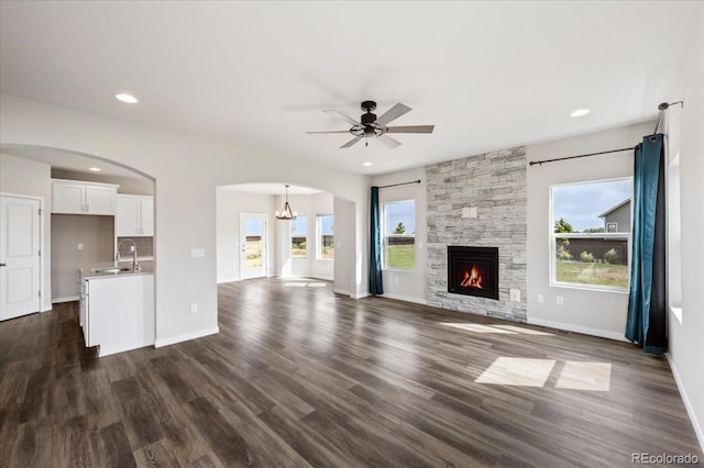 1711 Lazear St, Loveland, CO 80538 - unfurnished living room featuring a sink, arched walkways, ceiling fan, dark wood finished floors, and a stone fireplace