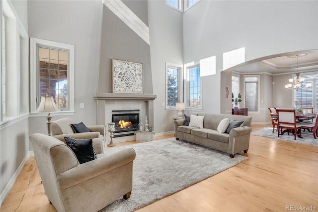 living room featuring a tile fireplace, a high ceiling, a raised ceiling, crown molding, and light hardwood / wood-style flooring