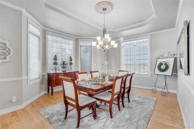 dining area featuring crown molding, an inviting chandelier, a tray ceiling, and light hardwood / wood-style floors