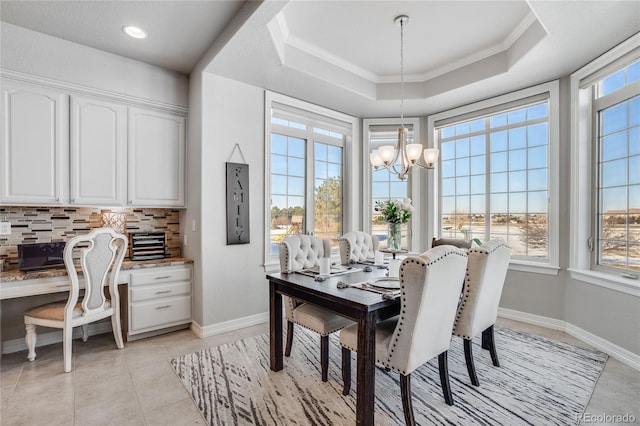 tiled dining space featuring a raised ceiling, ornamental molding, built in desk, and a chandelier