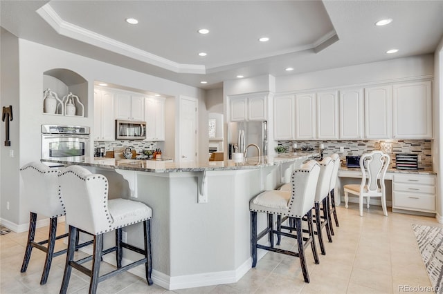 kitchen with appliances with stainless steel finishes, a raised ceiling, light stone countertops, and white cabinets