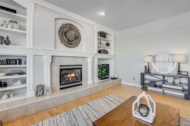 living room featuring ornamental molding, hardwood / wood-style floors, built in features, and a fireplace