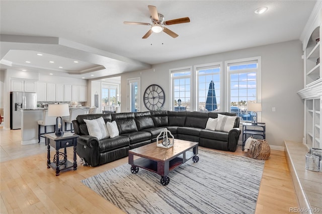 living room featuring a tray ceiling, ceiling fan, and light wood-type flooring