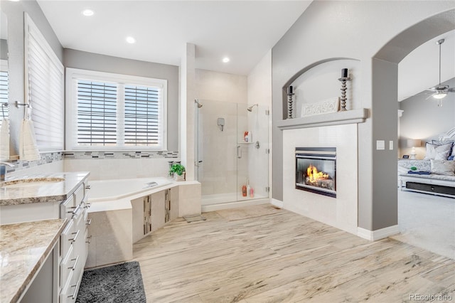 bathroom with hardwood / wood-style flooring, ceiling fan, vanity, a fireplace, and independent shower and bath