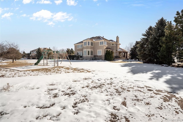 snow covered back of property featuring a playground