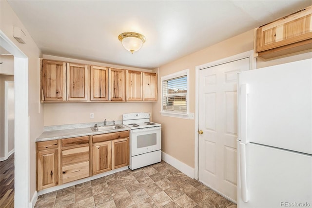 kitchen featuring light countertops, light brown cabinetry, a sink, white appliances, and baseboards