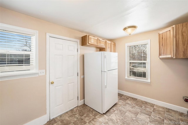 kitchen featuring light brown cabinetry, freestanding refrigerator, and baseboards