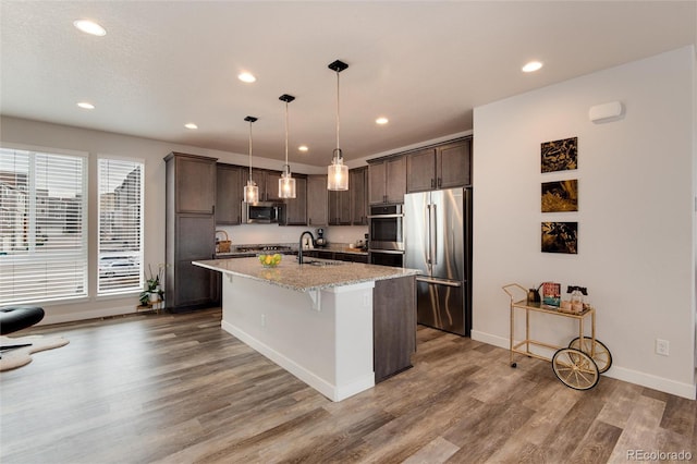 kitchen with pendant lighting, a breakfast bar, a kitchen island with sink, appliances with stainless steel finishes, and dark brown cabinetry