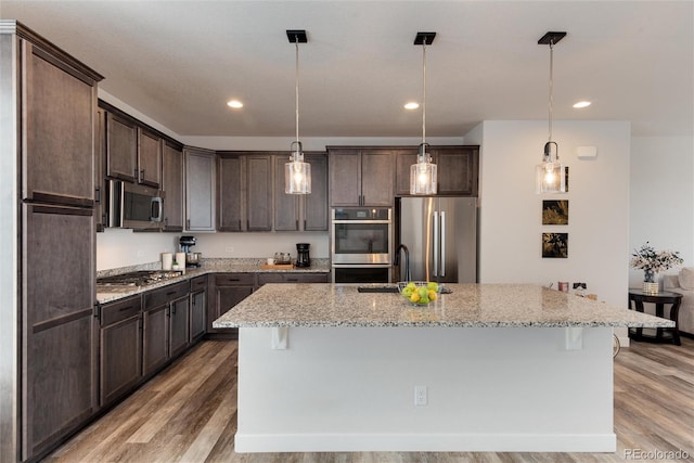 kitchen featuring light stone countertops, a kitchen island with sink, stainless steel appliances, and decorative light fixtures