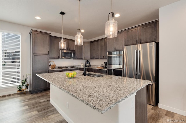 kitchen featuring light stone countertops, appliances with stainless steel finishes, sink, a center island with sink, and hanging light fixtures