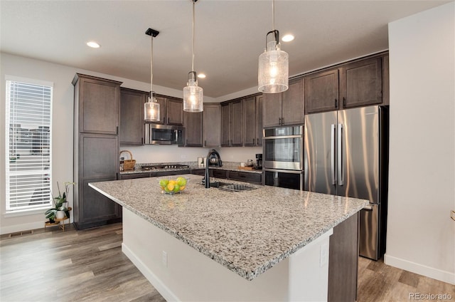 kitchen featuring pendant lighting, a kitchen island with sink, sink, light stone countertops, and stainless steel appliances