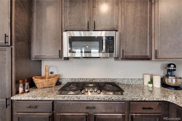 kitchen with light stone countertops, dark brown cabinets, and stainless steel appliances