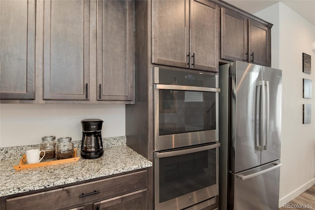 kitchen with appliances with stainless steel finishes, dark brown cabinetry, light stone counters, and hardwood / wood-style floors