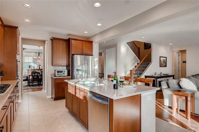 kitchen with open floor plan, brown cabinets, a sink, appliances with stainless steel finishes, and light tile patterned floors
