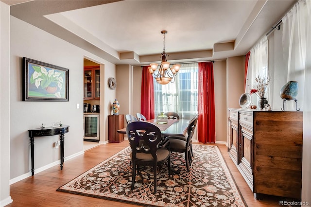 dining space featuring beverage cooler, baseboards, a tray ceiling, light wood-style flooring, and a notable chandelier
