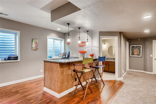 kitchen featuring light stone counters, a breakfast bar area, a textured ceiling, a peninsula, and light wood-type flooring