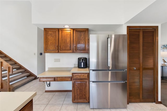kitchen featuring freestanding refrigerator, light tile patterned floors, light countertops, and brown cabinets