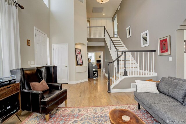 living area featuring visible vents, a towering ceiling, wood finished floors, stairway, and baseboards
