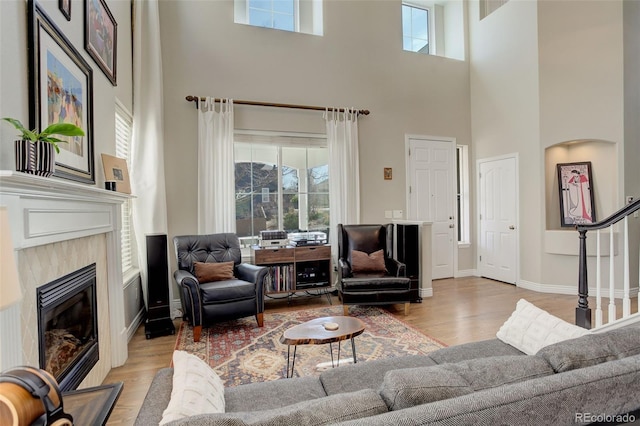 living room featuring a glass covered fireplace, light wood-style flooring, and a towering ceiling