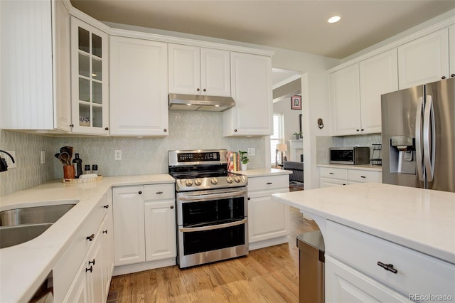 kitchen featuring appliances with stainless steel finishes, a sink, backsplash, white cabinetry, and under cabinet range hood