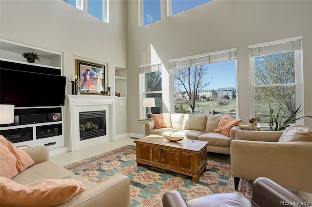 living room featuring a glass covered fireplace, built in shelves, and a towering ceiling