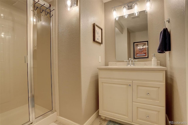 bathroom featuring vanity, a textured wall, baseboards, and a stall shower
