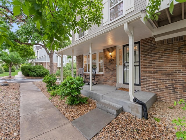 entrance to property featuring a porch and brick siding